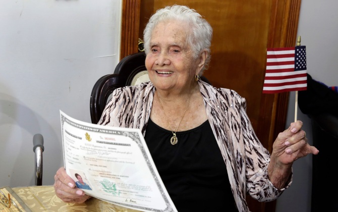 America Maria Hernandez, 99, holds an American flag after being administered the Naturalization Oath of Allegiance, Wednesday, Nov. 23, 2016 photo, in the Queens borough of New York. The Colombian immigrant, who was brought to the U.S. by one of her daughters in 1988, signed her naturalization certificate and took the oath of allegiance in her living room, surrounded by family members and TV cameras. (AP Photo/Richard Drew)
